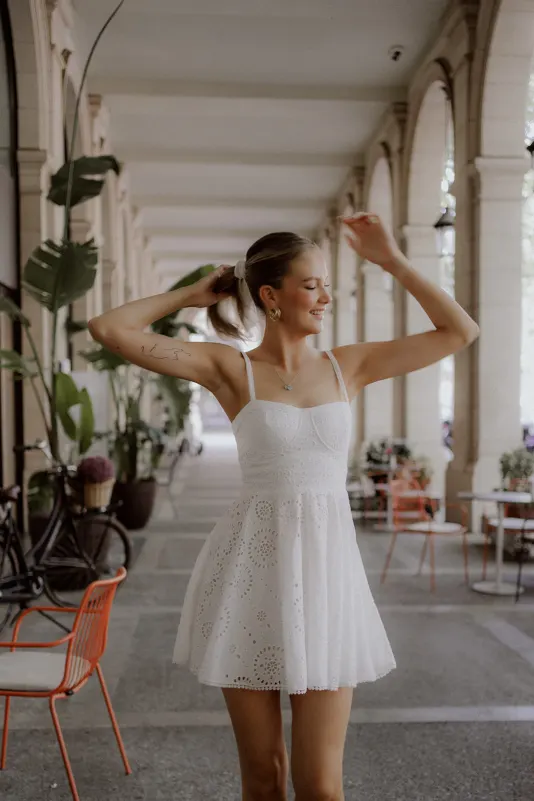 Woman in a white dress smiles and dances under city arches, Vacation Portraits photoshoot capturing carefree joy.