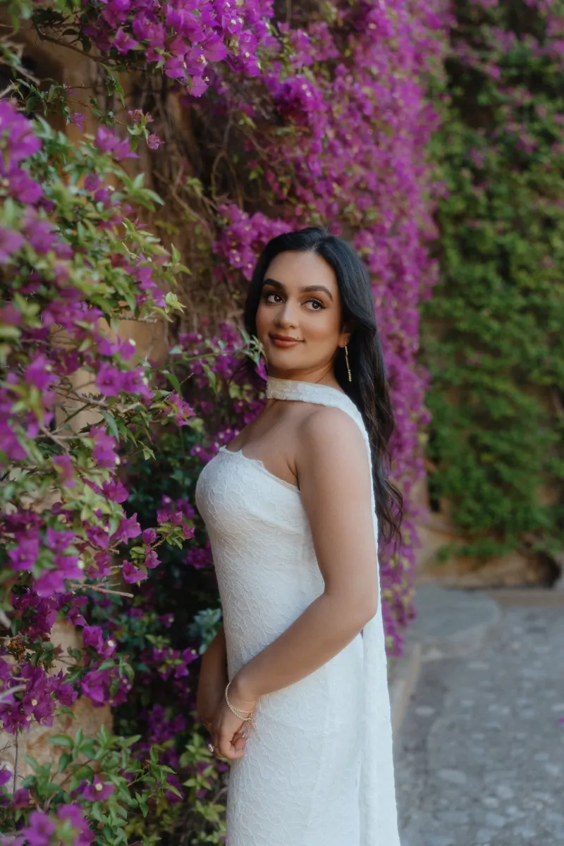 Woman in a white dress smiles softly beside vibrant bougainvillea during a surprise proposal photoshoot.