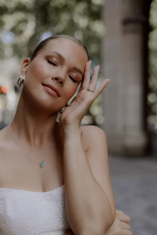 Woman in a white dress smiles softly with closed eyes, Vacation Portraits photoshoot capturing a peaceful city moment.
