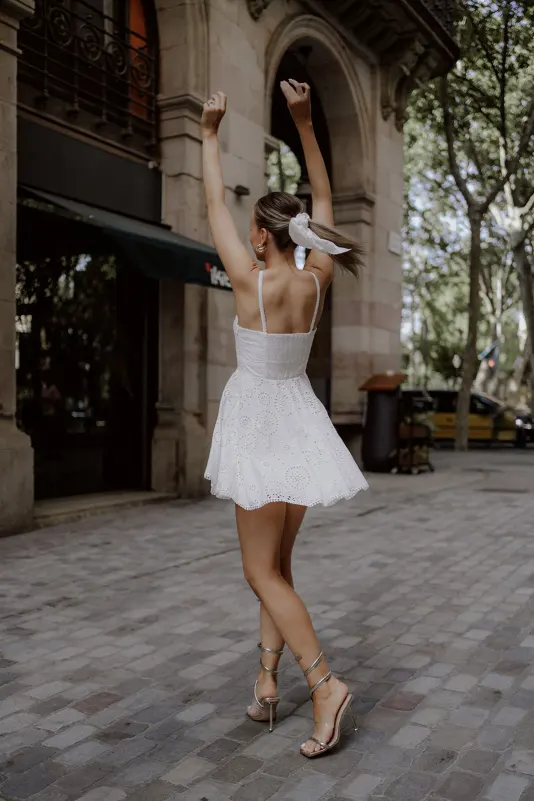 Woman in a white dress twirls joyfully on a cobblestone street, Vacation Portraits photoshoot in a European city.