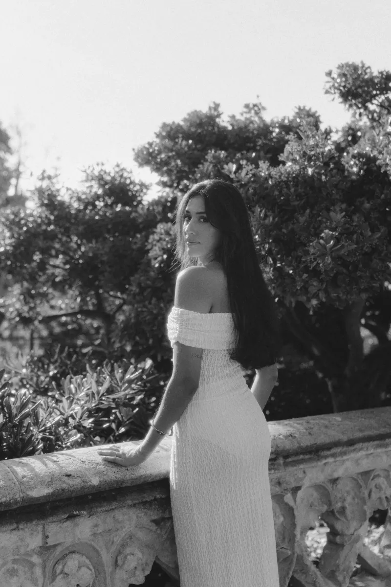 Woman in an off-shoulder dress stands by a stone railing, gazing softly back during a romantic outdoor session.