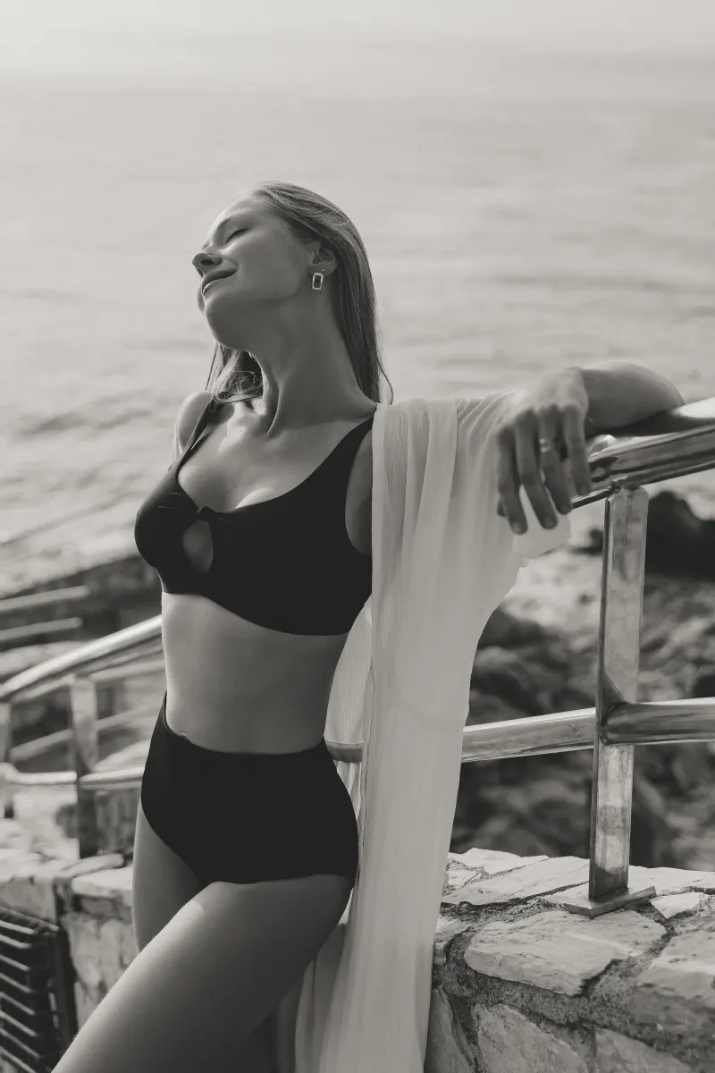 Woman in swimwear closes her eyes and smiles, savoring a peaceful seaside moment during a Vacation Portraits photoshoot.