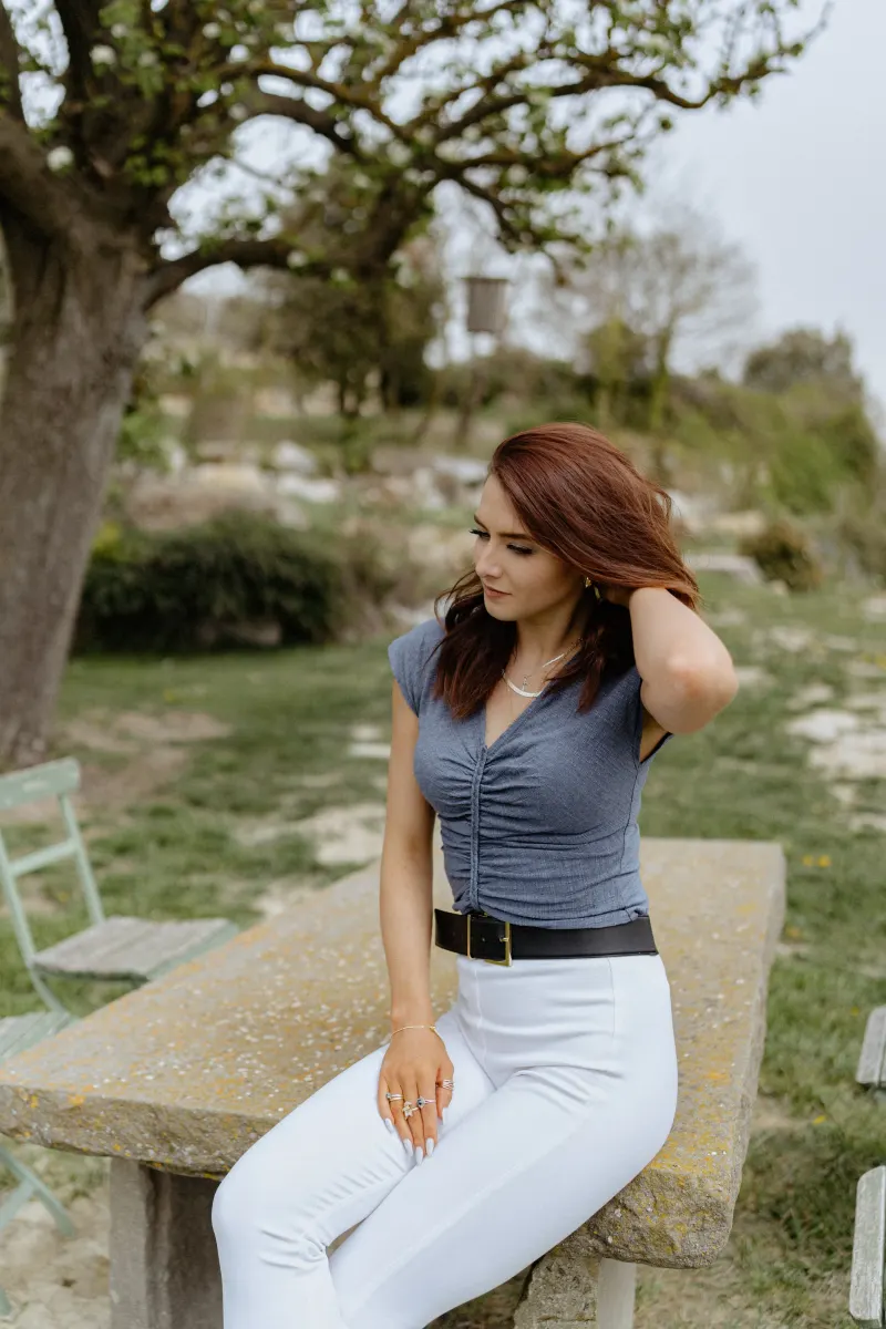 Woman sits thoughtfully at a stone picnic table in the countryside, awaiting a surprise proposal photoshoot.