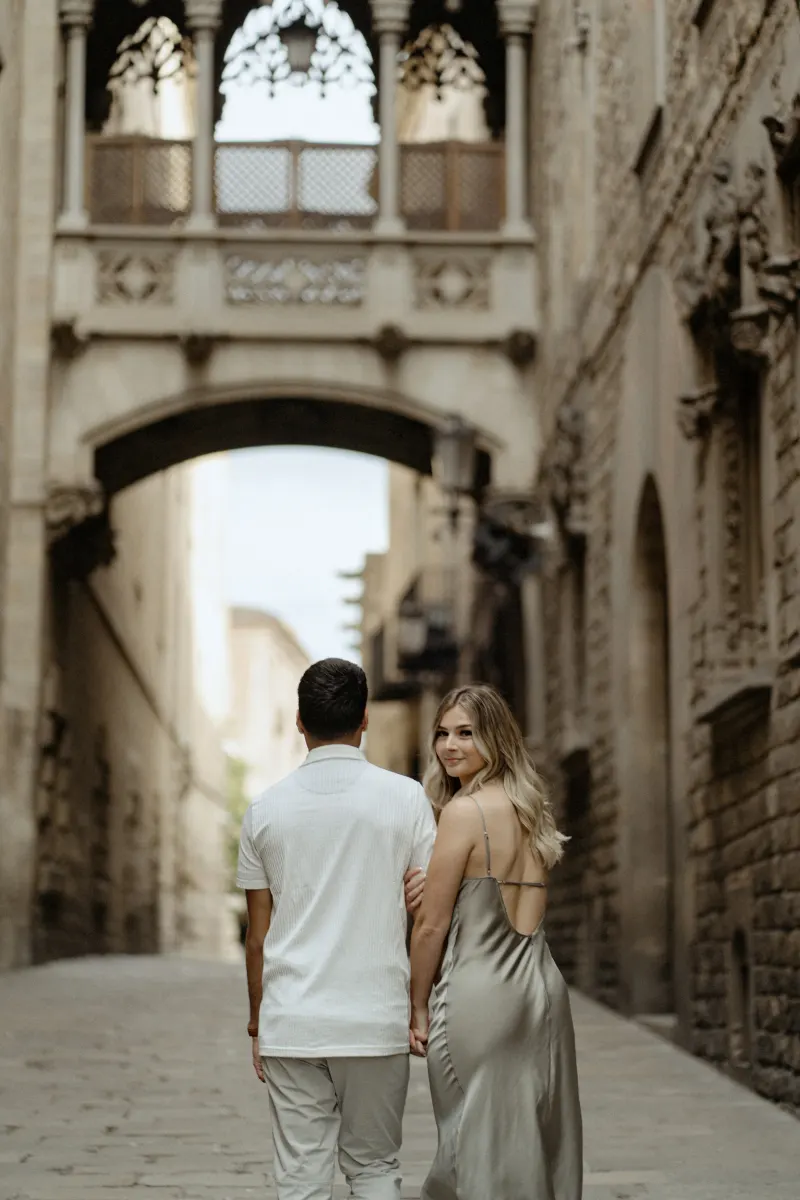 Woman smiles back at the camera while holding her partner’s hand in Barcelona’s Gothic Quarter during a Vacation Portraits sh