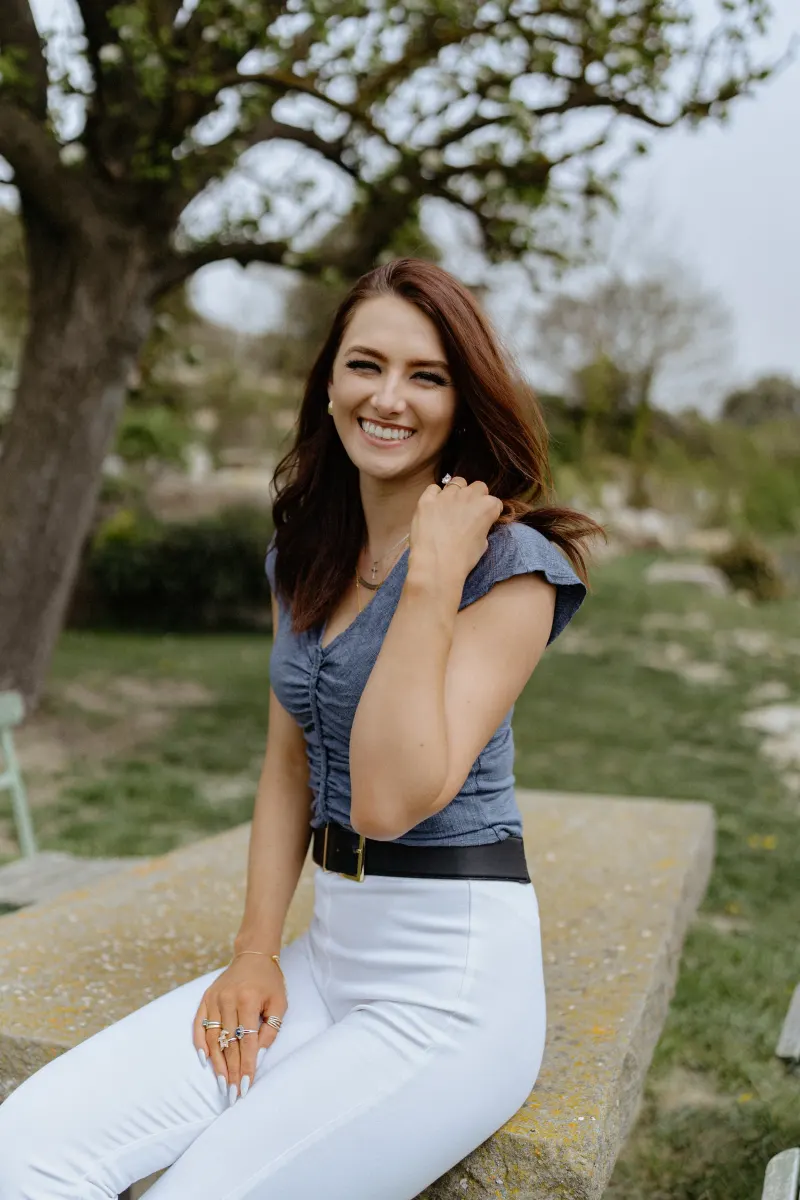 Woman smiles brightly while seated outdoors, capturing candid joy during a countryside surprise proposal photoshoot.