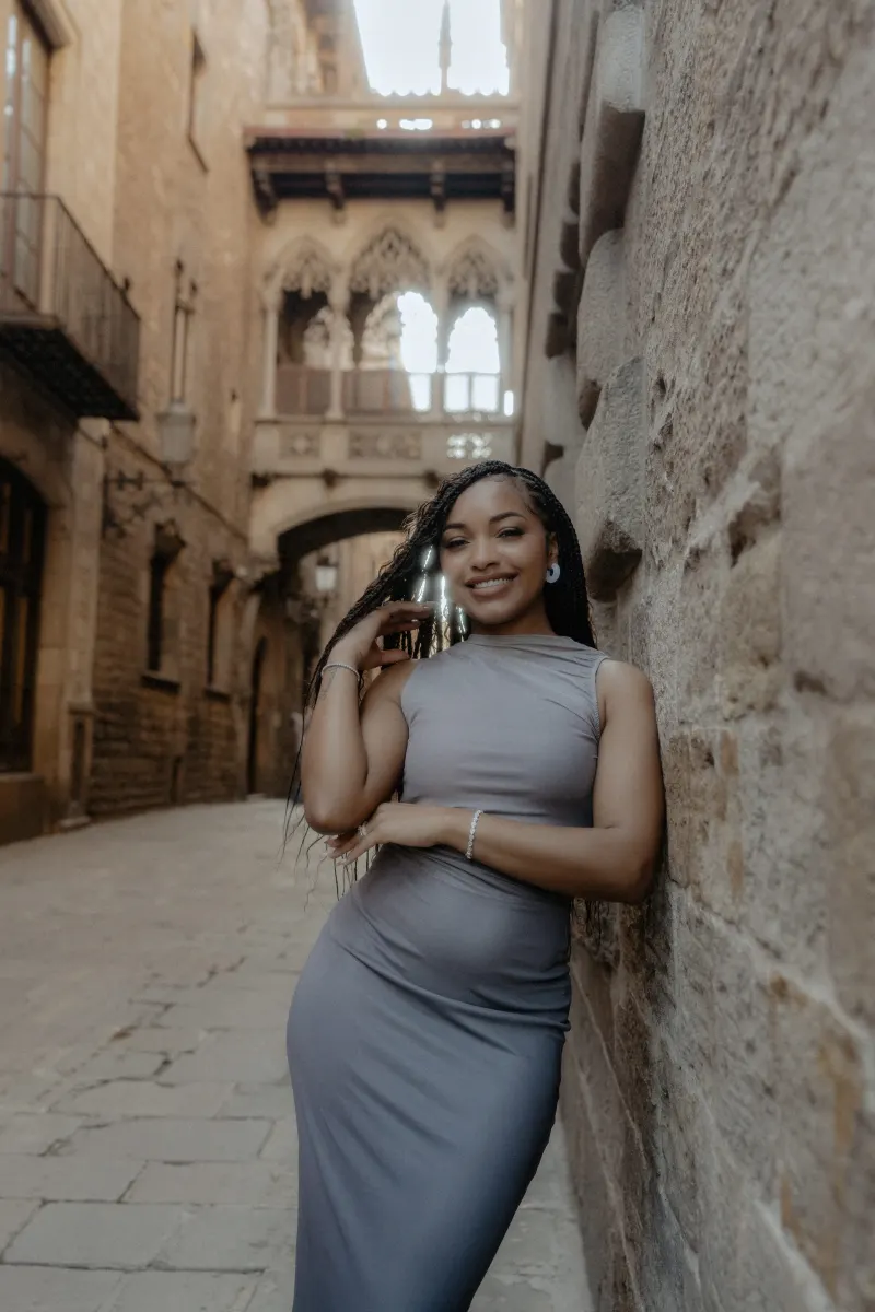Woman smiles warmly, leaning against a stone wall in Barcelona’s Gothic Quarter during a surprise proposal photoshoot.