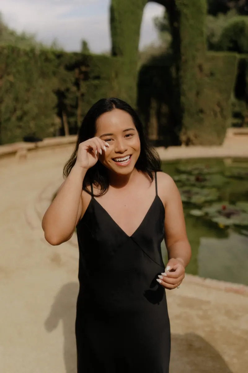 Woman wipes away happy tears by a lily pond after a surprise proposal, captured during a professional photoshoot.