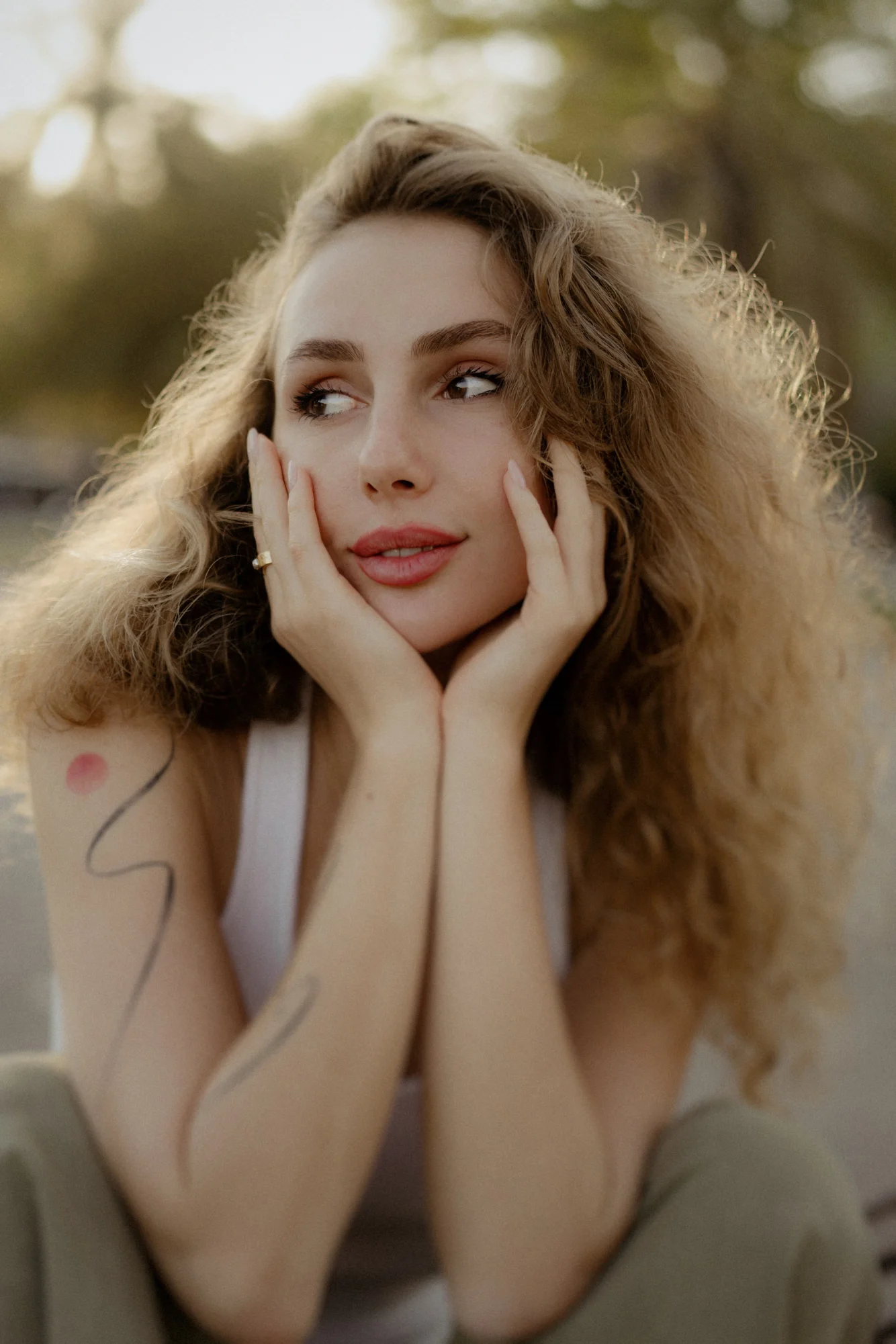Woman with curly hair rests her face in her hands, gazing away thoughtfully during a Vacation Portraits photoshoot outdoors.
