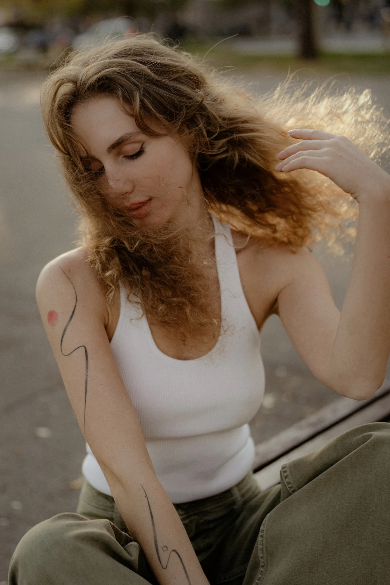 Woman with curly hair sits outdoors, eyes closed and smiling softly, during a relaxed Vacation Portraits photoshoot.