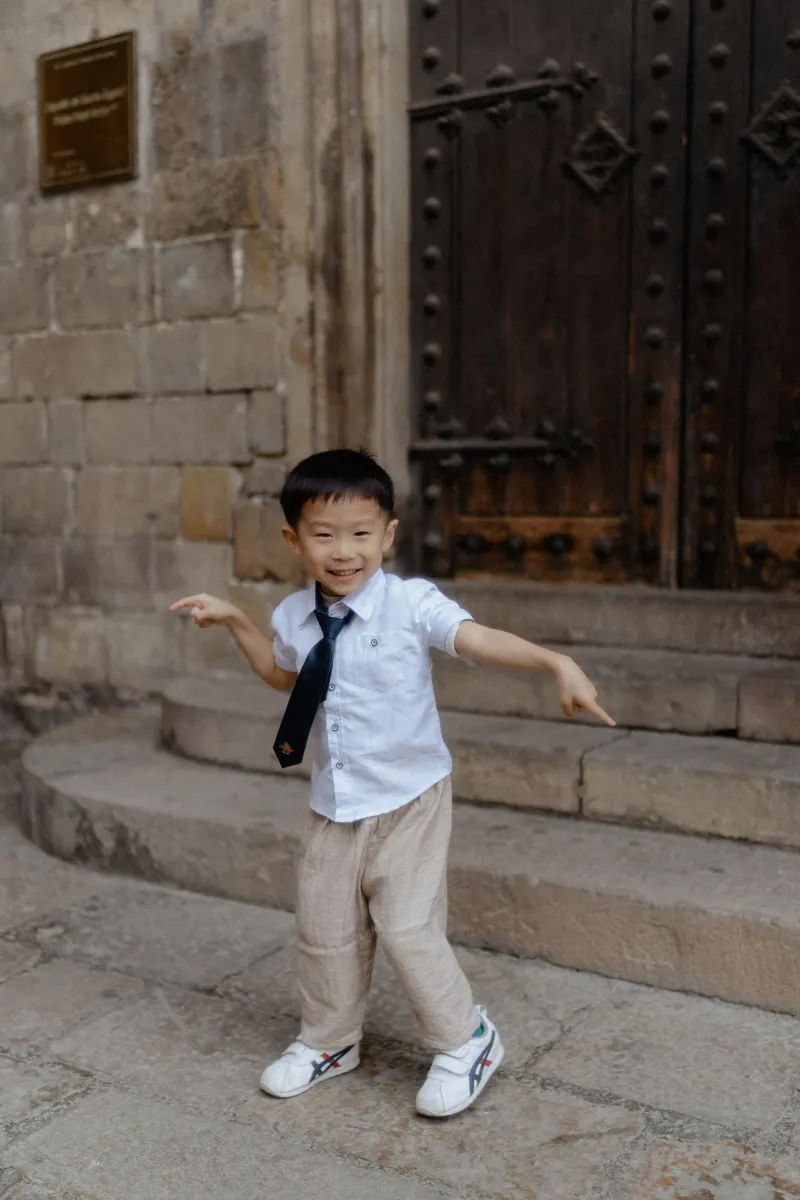 Young boy in a tie playfully poses on stone steps during a Vacation Portraits photoshoot in Barcelona’s Gothic Quarter.