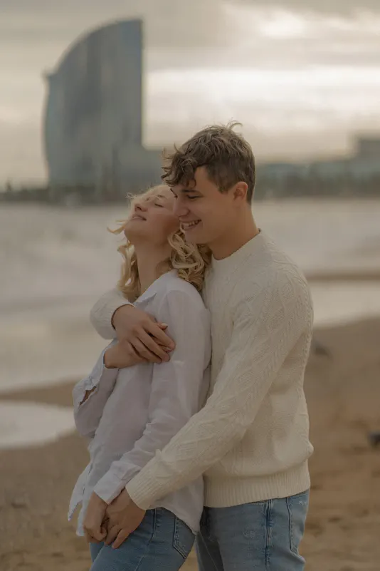 Young couple shares a joyful embrace on Barcelona beach during a couples & engagements photoshoot.