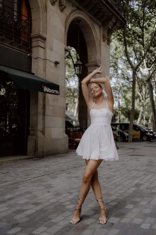 Young woman in a white dress dances with joy beneath city arches, Vacation Portraits photoshoot capturing summer vibes.
