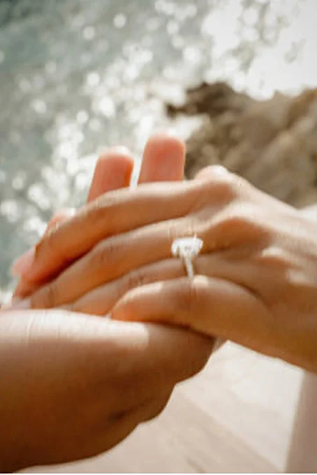A couple holds hands by the water in Barceloneta, showing an engagement ring and capturing a joyful moment.