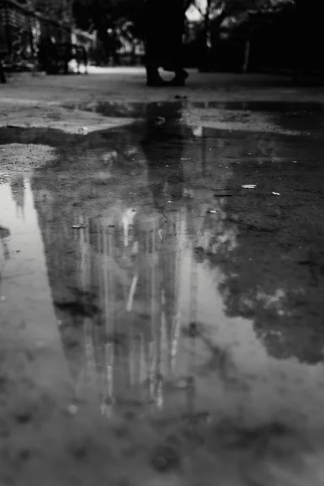 A passerby walks near a puddle reflecting La Sagrada Familia, capturing a quiet moment in Barcelona.