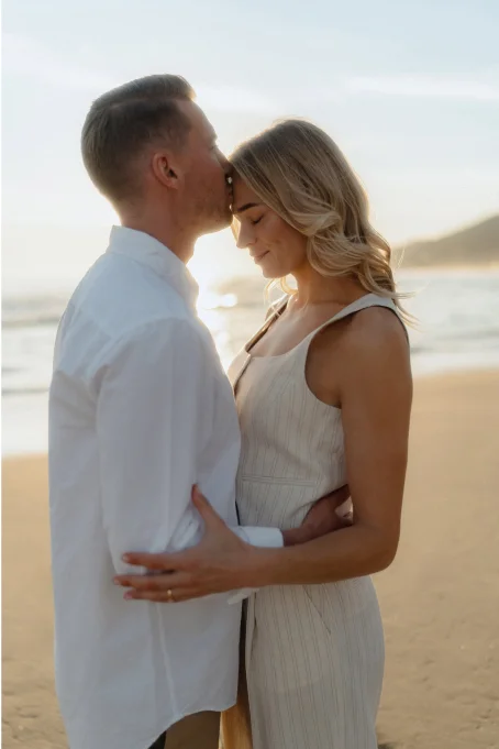 Couple embraces at sunset on Barceloneta beach, sharing a tender moment during a romantic location photoshoot.