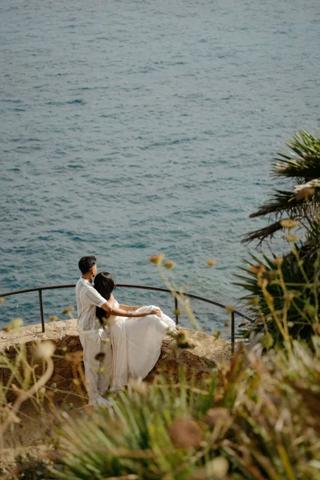 Couple embraces on a stone terrace overlooking the sea at Marimurtra garden, captured for a romantic location photoshoot.