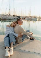 Couple embracing at Ginesta beach port, sharing a peaceful moment by the water during a sunset portrait session.