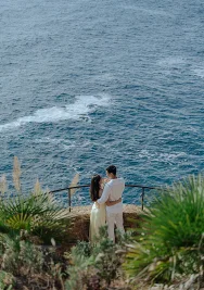 Couple embracing by the sea at Marimurtra Garden, sharing a romantic moment during a professional photo session.