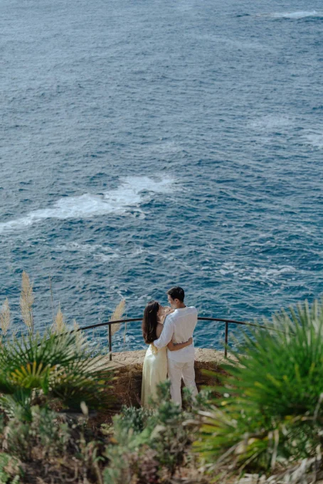 Couple embracing by the sea at Marimurtra garden, sharing a romantic moment for a location photography session.