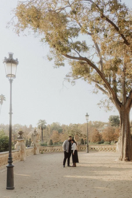 Couple embracing under autumn trees in Park de la Ciutadella, Barcelona, captured during a romantic location photoshoot.