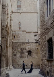 Couple holding hands and smiling as they walk through a quiet Gothic Quarter alley, perfect for engagement photography.