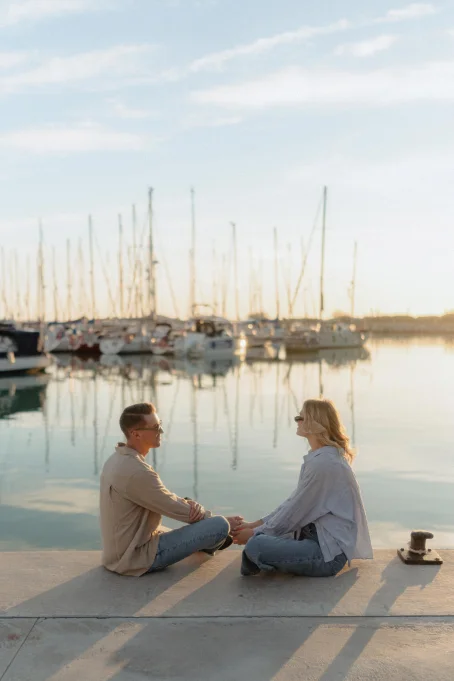 Couple holding hands and smiling at Ginesta port, captured during a golden hour location photography session.