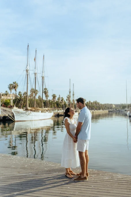 Couple holding hands and smiling by the water at Port Vell, Barceloneta, perfect for romantic location photography sessions.