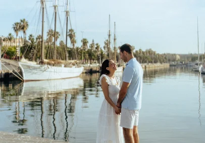 Couple holding hands and smiling by the water at Port Vell, perfect for a romantic Barceloneta photoshoot session.