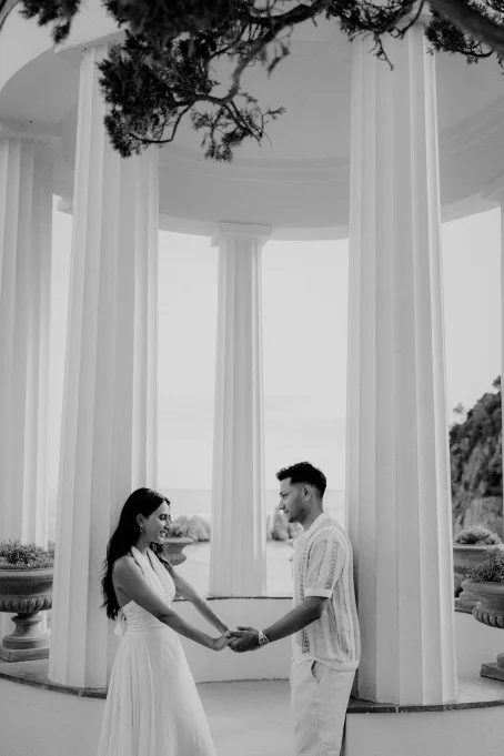 Couple holding hands and smiling under the columns at Marimurtra garden, captured during a romantic location photoshoot.