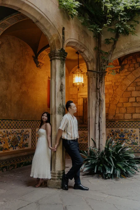 Couple holding hands around a column, sharing a romantic moment in the Gothic Quarter for a location portrait session.