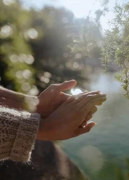 Couple holding hands by the water at Park de la Ciutadella, sunlight highlighting an engagement ring.