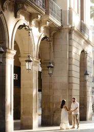 Couple holding hands under sunlit arches in the Gothic Quarter, perfect for an engagement photography session.
