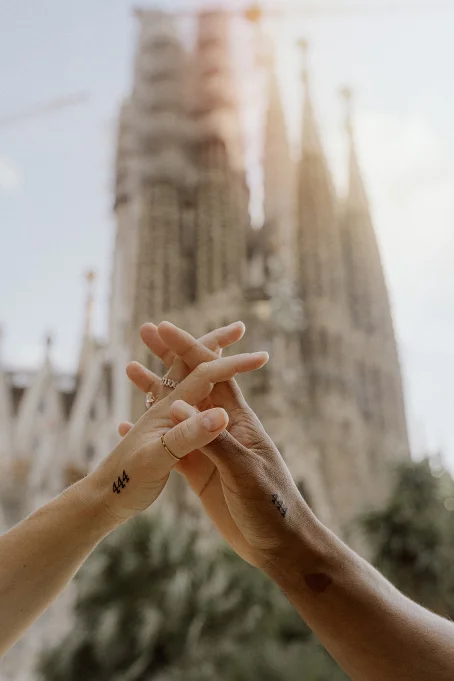 Couple holding hands with matching tattoos in front of La Sagrada Familia, captured during a location photography session.