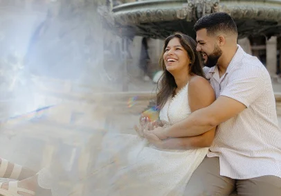 Couple laughing and embracing by a fountain in the Gothic Quarter, captured during a romantic portrait session.