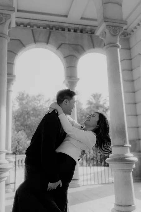 Couple laughing and embracing under stone arches at Park de la Ciutadella, captured during a romantic location photoshoot.