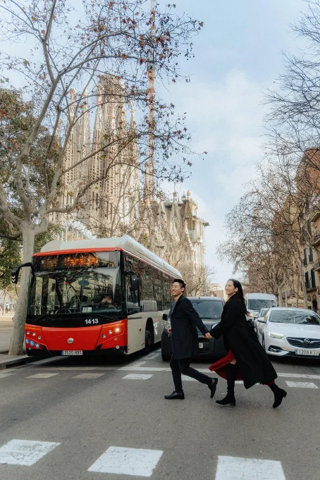 Couple laughing and holding hands while crossing the street near La Sagrada Familia, captured by a professional photographer.