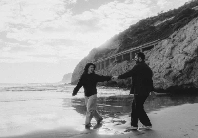 Couple laughing and holding hands while walking along Ginesta beach, perfect for candid engagement photography sessions.