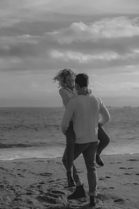 Couple laughing as he lifts her on Barceloneta beach, capturing candid joy for a location photography session.