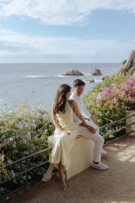 Couple sharing a quiet moment by the sea at Marimurtra garden, surrounded by flowers and scenic coastal views.