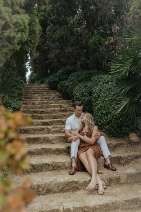 Couple sharing a tender moment on stone steps surrounded by lush greenery at Marimurtra garden, location photography session.