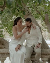Couple sharing an intimate moment on a stone bench under lush trees at Park de la Ciutadella, engagement photography.