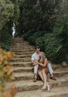 Couple sharing an intimate moment on stone steps surrounded by lush greenery at Marimurtra Garden, engagement photography.