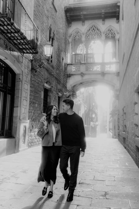 Couple walking arm in arm and smiling in the sunlit Gothic Quarter, perfect for romantic location photography sessions.