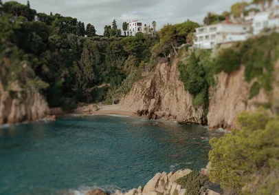 Dramatic coastal cliffs and lush greenery surround a secluded beach at Marimurtra Garden, perfect for destination shoots.