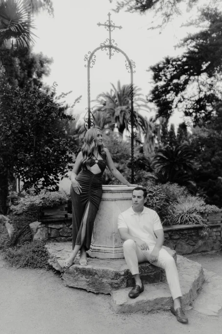 Elegant couple poses by a stone well in Marimurtra garden, capturing a timeless moment for a location portrait session.