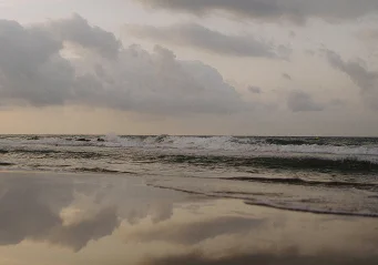 Gentle waves and moody clouds reflect on Barceloneta beach at dusk, capturing serene seaside moments in Barcelona.