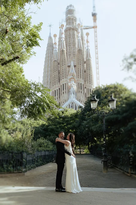 Joyful couple embraces in front of La Sagrada Familia, captured during a romantic location photography session.