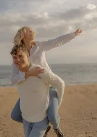 Joyful couple enjoying a playful piggyback ride on Barceloneta beach, perfect for couples photography sessions.