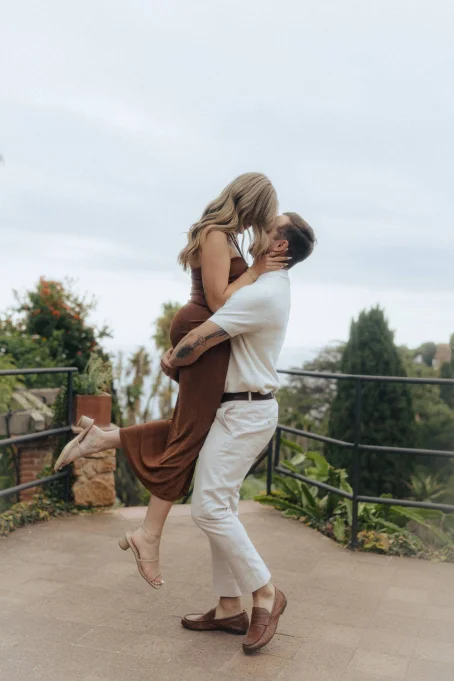 Joyful couple shares a kiss as he lifts her in Marimurtra garden, captured by a professional photographer.