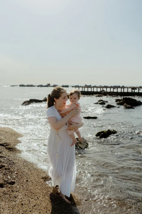 Mother and baby share a joyful moment by the water at Barceloneta beach, captured during a family photography session.